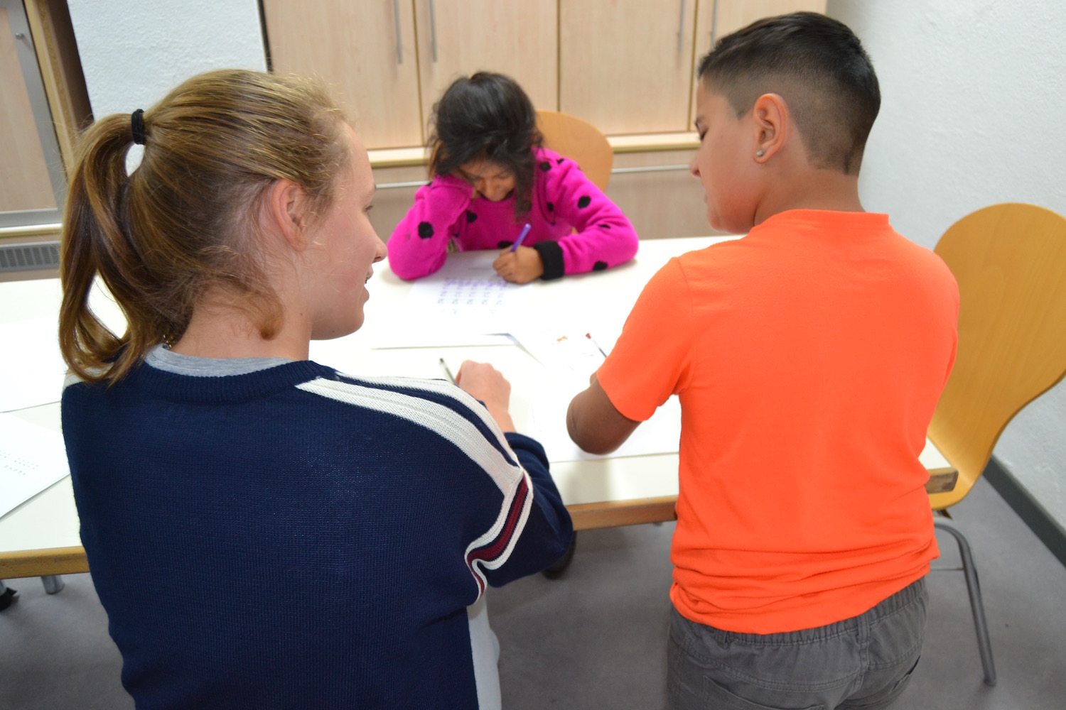 Een jongere helpt twee Romakinderen met hun huiswerk.