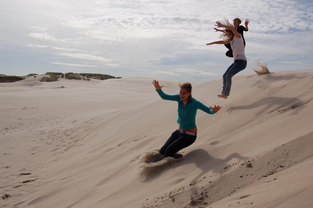 Jongeren springen van een zandduin